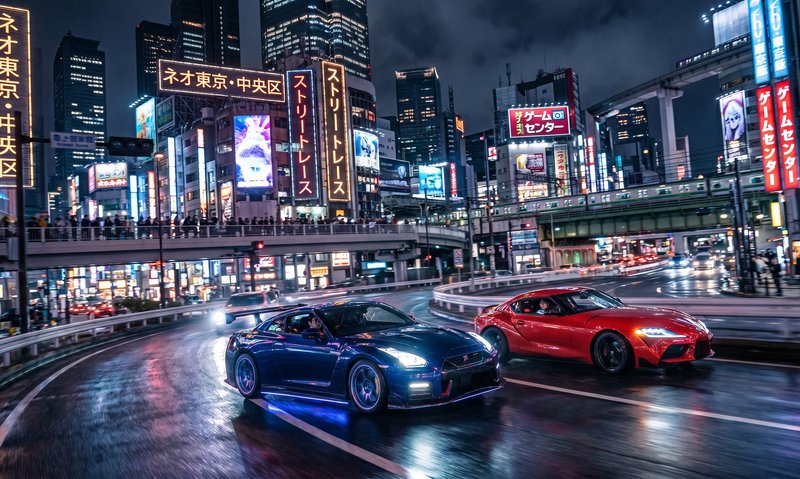 Two sports cars race through a neon-lit city street at night