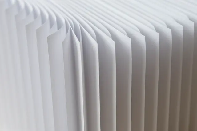 Full frame close-up of sharp parallel accordion folds in white paper catching soft diffused light