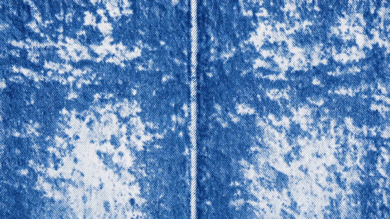 Full frame close-up of mottled acid wash blue denim fabric with a central stitched seam