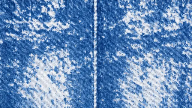 Full frame close-up of mottled acid wash blue denim fabric with a central stitched seam
