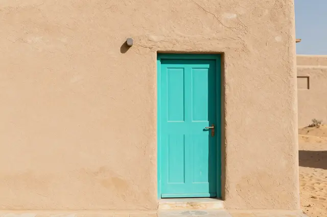 Turquoise front door set into a textured tan adobe wall in a sunny desert setting