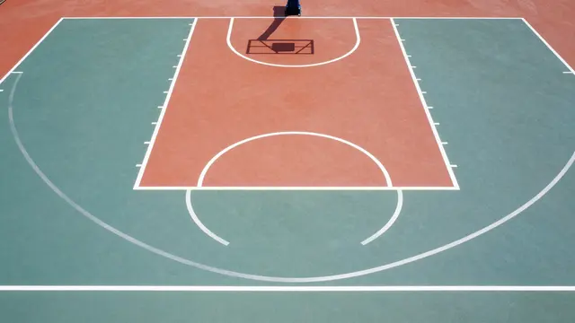 Overhead view of a brightly painted outdoor basketball court with red, teal and white line markings.