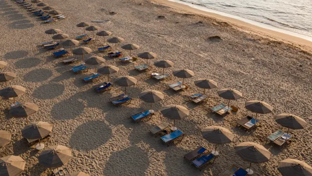 Aerial view of empty beach umbrellas and sun loungers casting long shadows on a sandy shore at sunset near gentle ocean