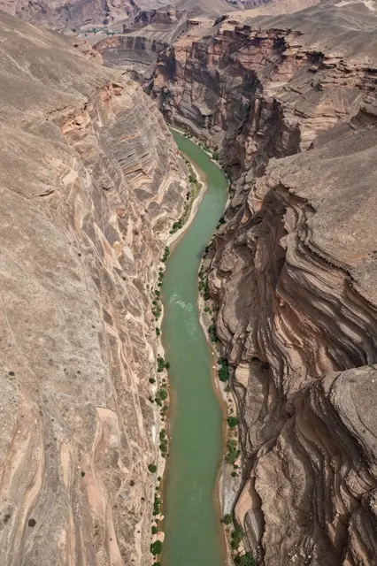 High angle aerial view of a narrow winding green river running through a deep layered desert canyon