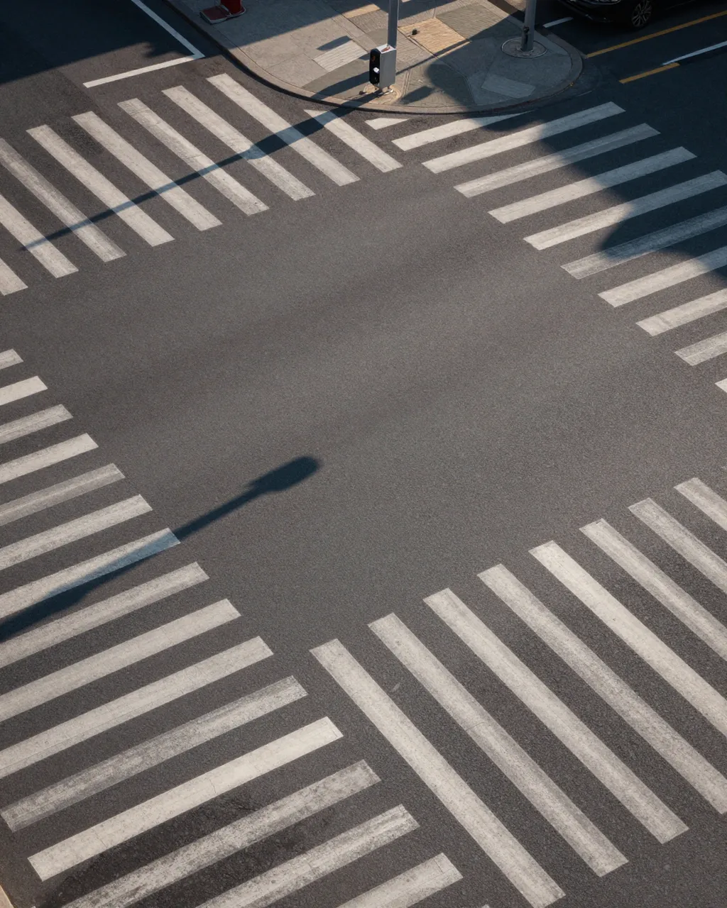 High angle view of an empty street intersection with crosswalk stripes and long evening shadows.