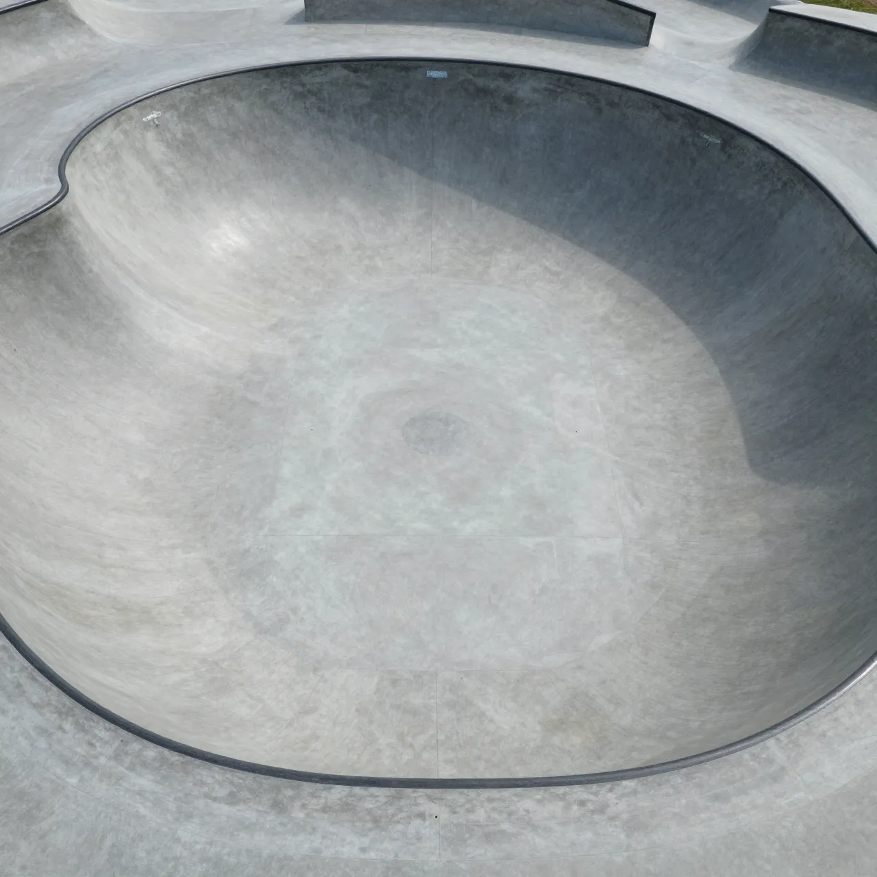 Top-down aerial view of a smooth empty concrete skate park bowl in bright daylight