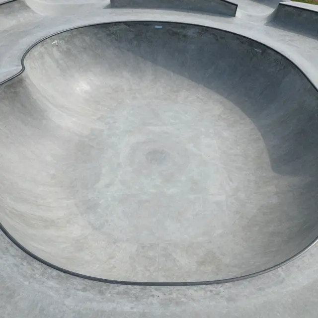 Top-down aerial view of a smooth empty concrete skate park bowl in bright daylight