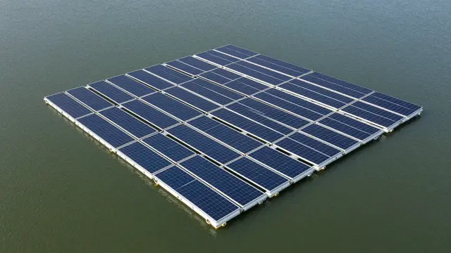 A grid of floating solar panels sits on calm green lake water viewed from above