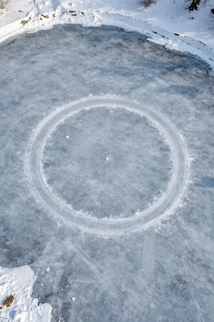 Overhead view of a frozen pond with a swept circular skating track bordered by snowbanks