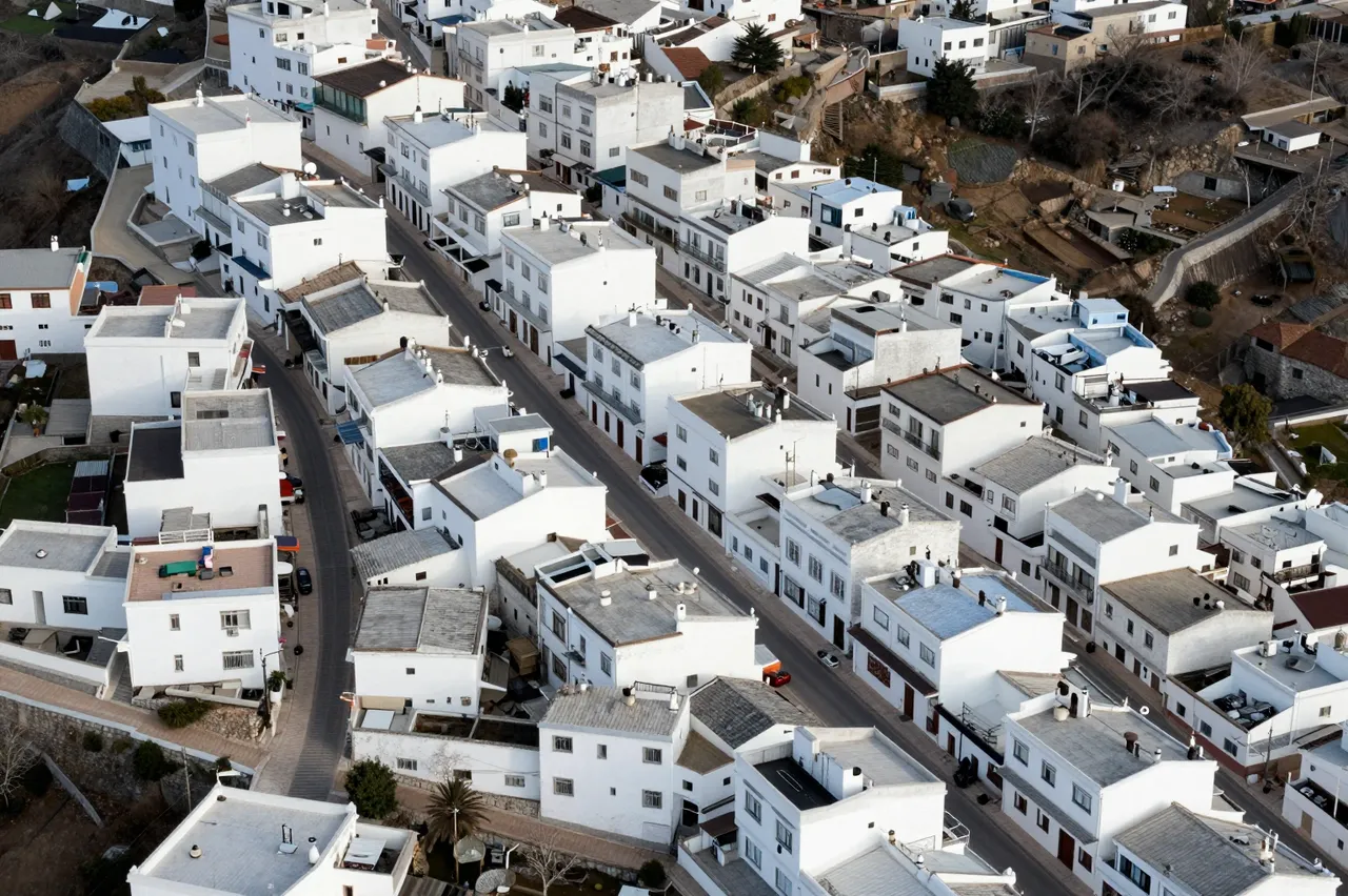 High angle aerial view of a dense hilltop village with clustered white flat-roofed houses and narrow paved streets