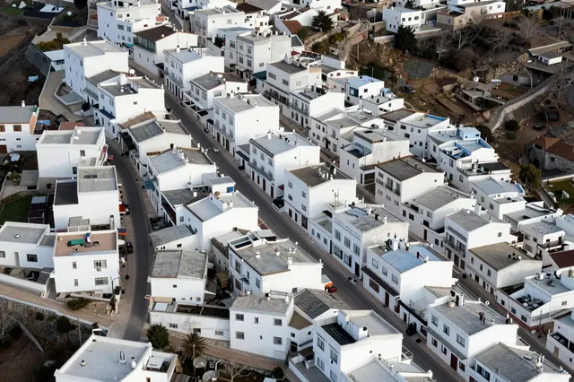 High angle aerial view of a dense hilltop village with clustered white flat-roofed houses and narrow paved streets