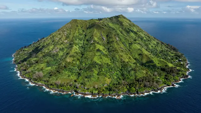 A high aerial view of a lush green volcanic island rising from a deep blue ocean under a partly cloudy sky