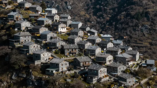 Aerial view of clustered stone houses built along a high mountain ridge under bright sunlight