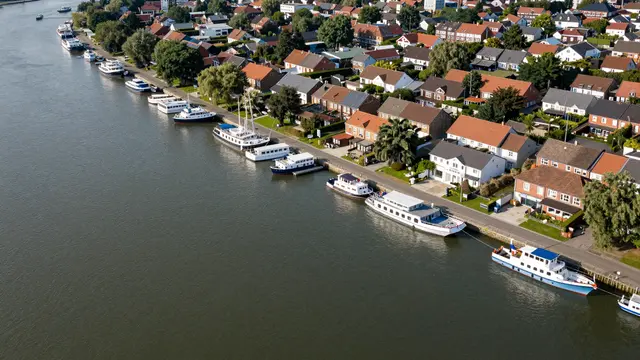 Aerial view of a riverside town with a line of moored boats along a tree-lined residential bank