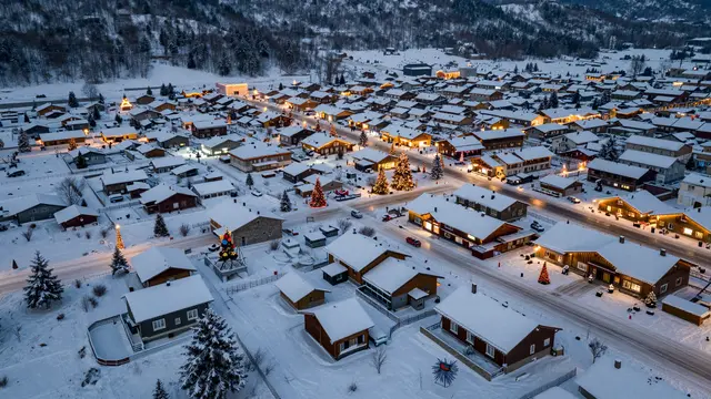 Aerial night view of a snow-covered mountain village decorated with glowing Christmas lights and lit windows