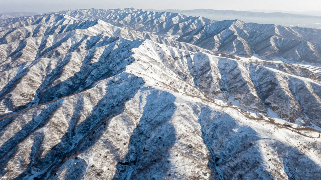 Aerial view of sunlit, snow-dusted mountain ridges stretching across a hazy winter landscape