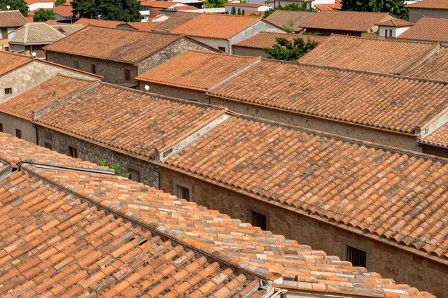 High angle view of overlapping weathered terracotta tile rooftops across a historic stone old town.