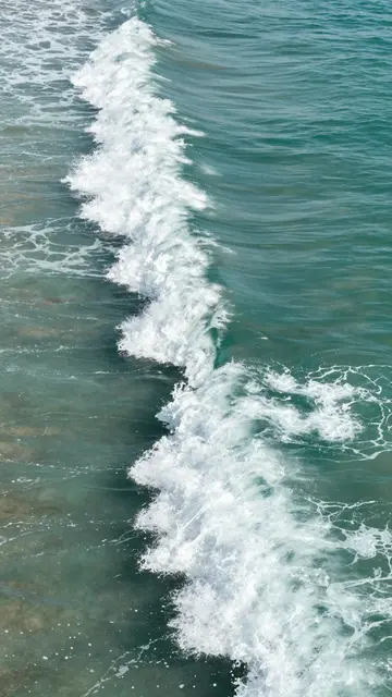 Overhead view of curling turquoise ocean waves topped with bright white seafoam