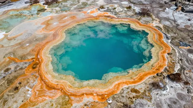 Top down aerial view of a hot spring with vivid turquoise water and layered orange mineral rings