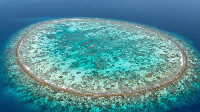 High angle aerial view of a ring-shaped coral atoll surrounded by deep blue open ocean