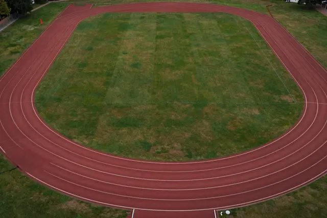 Top-down aerial view of an empty red running track surrounding a grass sports field at a recreation ground.