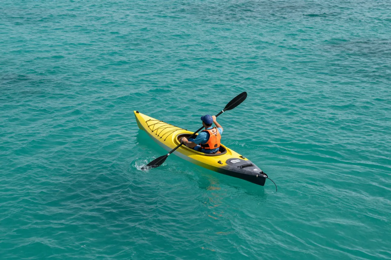 Overhead view of a person paddling a yellow kayak across bright turquoise ocean water