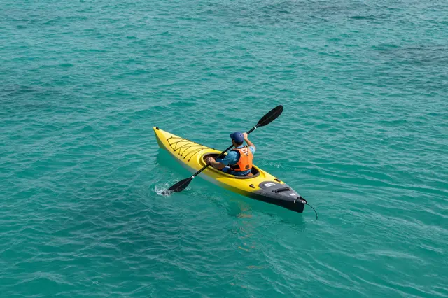 Overhead view of a person paddling a yellow kayak across bright turquoise ocean water