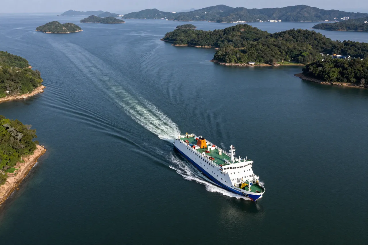 A high angle view of a passenger ferry moving through dark blue water between forested green islands, leaving a curved wake