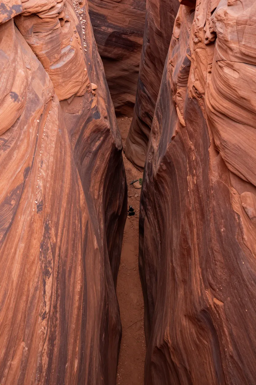 High angle aerial view looking down into a narrow winding red rock slot canyon