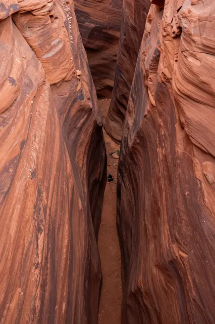 High angle aerial view looking down into a narrow winding red rock slot canyon