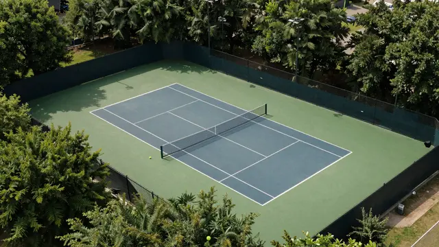 Overhead aerial view of an empty tennis court enclosed by fencing and dense leafy trees