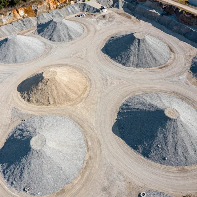 Top-down aerial shot of conical sand and gravel piles in a sunlit quarry with long distinct shadows.