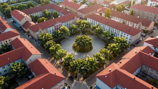 Aerial sunrise view of a leafy central square surrounded by uniform red-roofed city apartment blocks