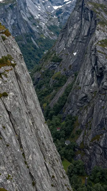 High-angle vertical view of a narrow mountain valley between sheer gray rocky cliffs with forest below