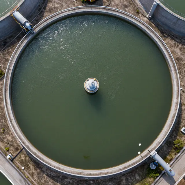 Top-down aerial view of a large circular water treatment tank with rippling green water at an industrial facility