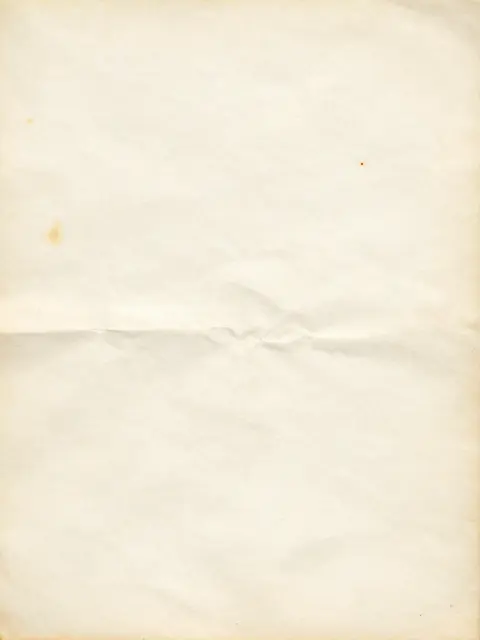 Full frame close-up of aged ivory paper with faint rust spots, soft creases, and even diffused lighting