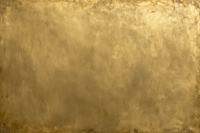 Full frame close-up of worn aged brass surface with uneven dark tarnish and subtle scratch marks