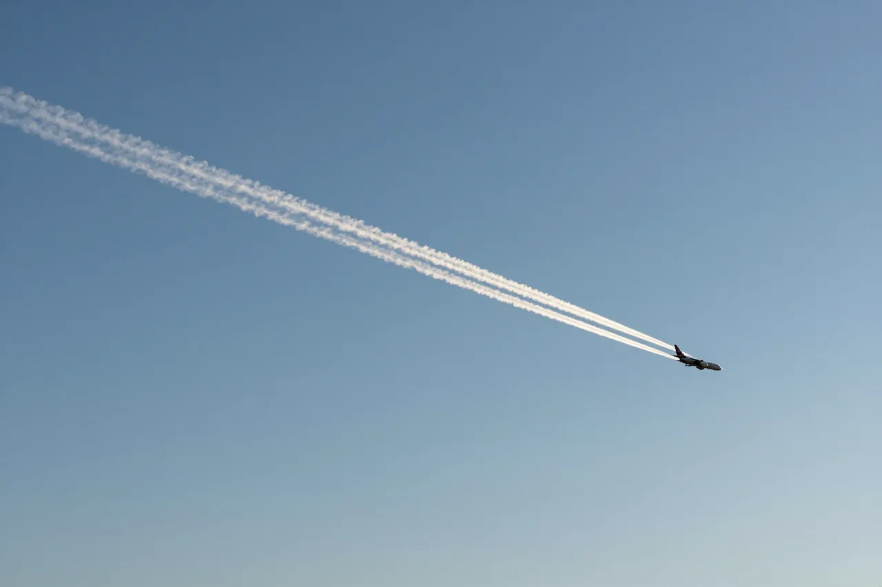 A small jet airliner flies leaving a long white contrail across a clear bright blue sky