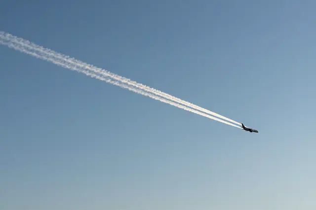 A small jet airliner flies leaving a long white contrail across a clear bright blue sky