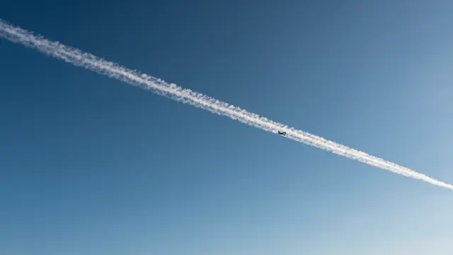 A small distant aircraft leaves a long white contrail streaking across a clear deep blue sky