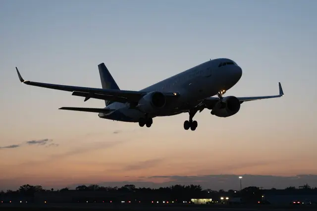 A commercial jet airliner on final approach to land over an airport runway at dusk