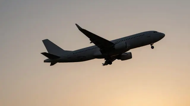 A commercial jet airplane flies with extended landing gear against a soft gradient sunset sky.
