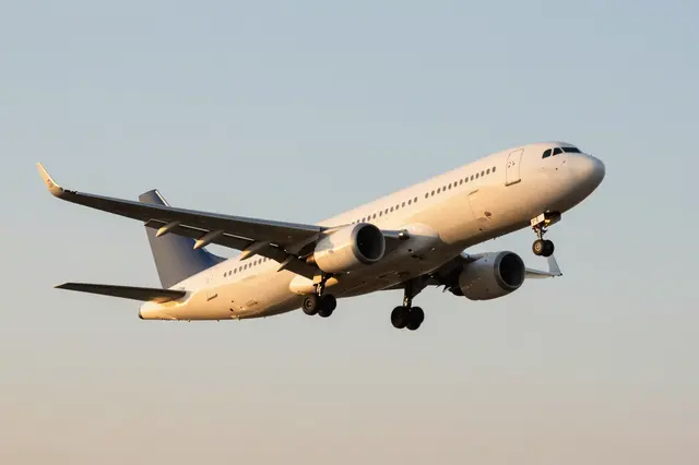 Unbranded commercial passenger airplane with extended landing gear climbs against a soft hazy sunset sky.