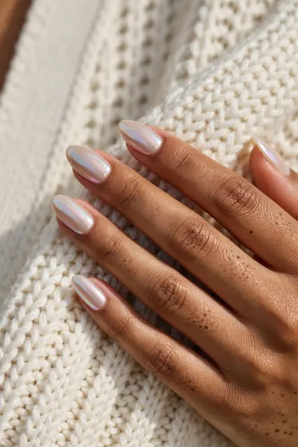 A hand with iridescent almond glazed pearl nails rests on an ivory knit cardigan