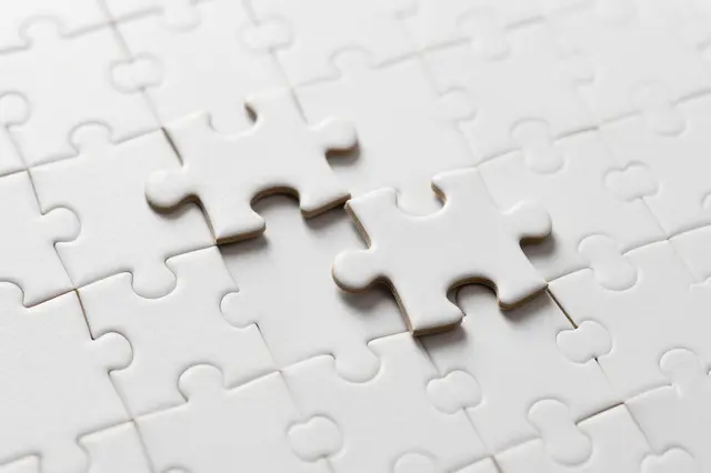 Two loose blank jigsaw pieces rest beside gaps in an otherwise completed plain white puzzle