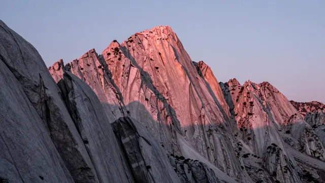 Jagged granite mountain peaks glow soft pink from alpenglow under a pale dawn sky