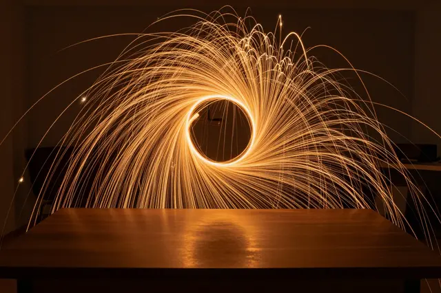 Long exposure circular amber light swirl arcs above an empty dark wooden desk in a dim room