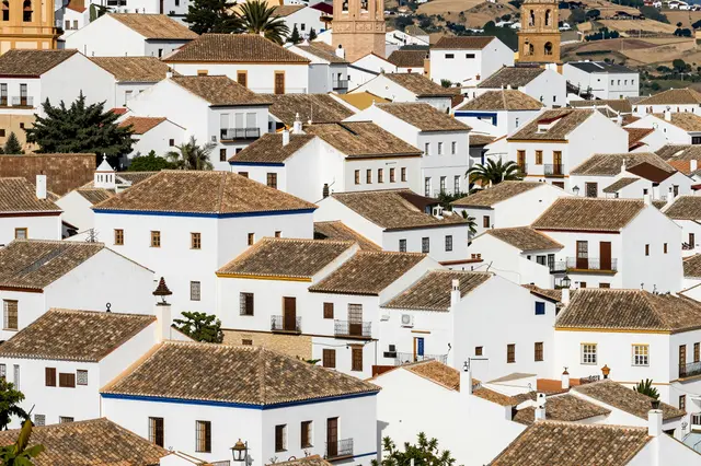 Densely clustered whitewashed Andalusian town buildings with terracotta tiled roofs set against rolling rural hills.