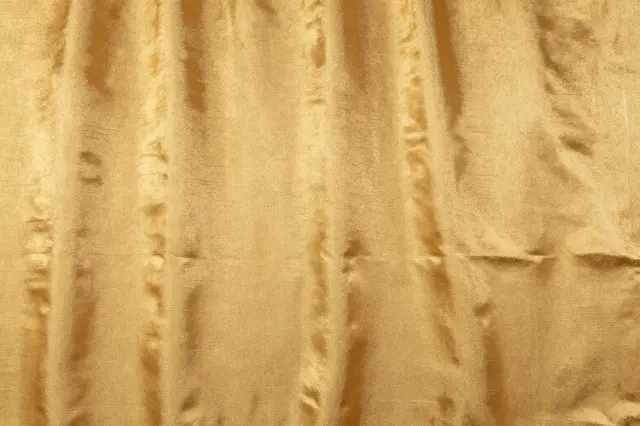Full frame close-up of crinkled antique gold dupioni silk fabric with natural slubs and soft sheen