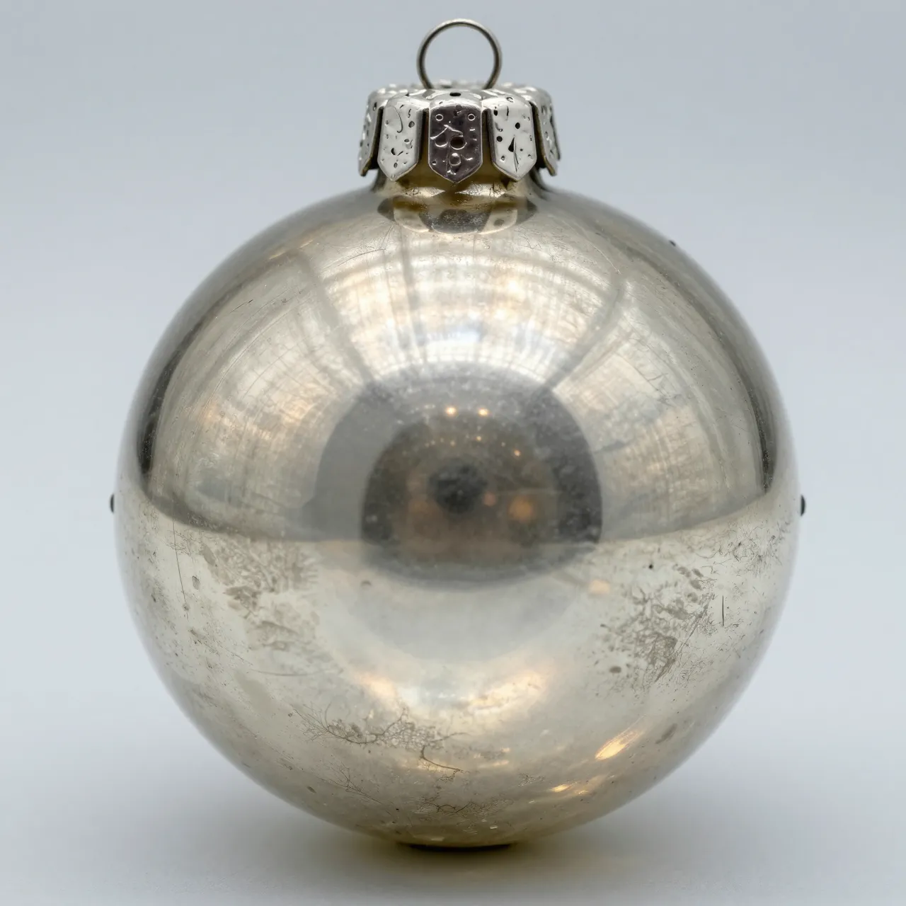 A close-up macro view of a worn vintage silver mercury glass Christmas ornament against a plain light gray background.